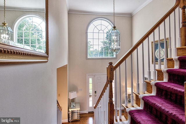 stairway featuring crown molding, plenty of natural light, hardwood / wood-style floors, and an inviting chandelier