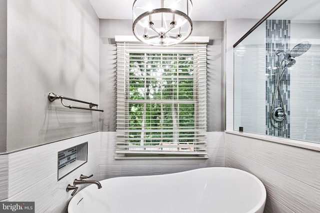 bathroom with plus walk in shower, a healthy amount of sunlight, tile walls, and a notable chandelier