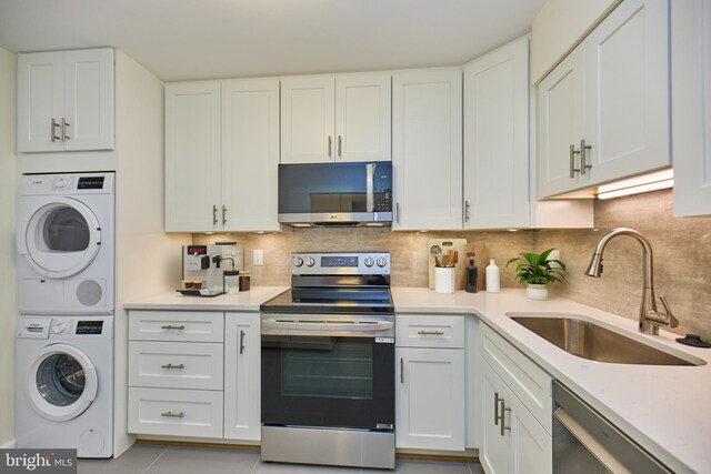 kitchen featuring appliances with stainless steel finishes, a sink, stacked washer / dryer, white cabinetry, and tasteful backsplash