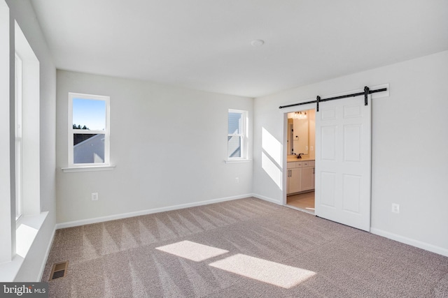 unfurnished bedroom featuring ensuite bath, a barn door, and light colored carpet