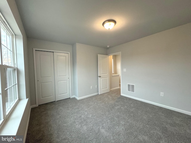 unfurnished bedroom with dark carpet and a closet