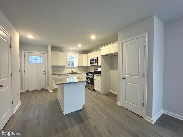 kitchen with light stone countertops, appliances with stainless steel finishes, white cabinets, dark hardwood / wood-style floors, and a kitchen island