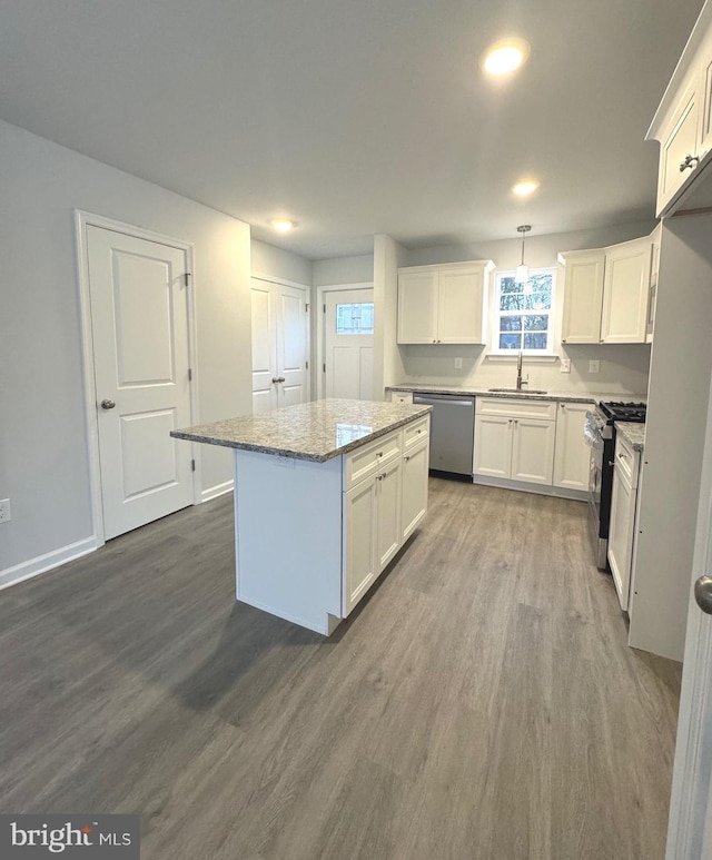 kitchen with sink, appliances with stainless steel finishes, decorative light fixtures, a kitchen island, and wood-type flooring