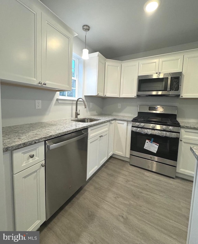 kitchen with stainless steel appliances, sink, white cabinets, hardwood / wood-style floors, and hanging light fixtures