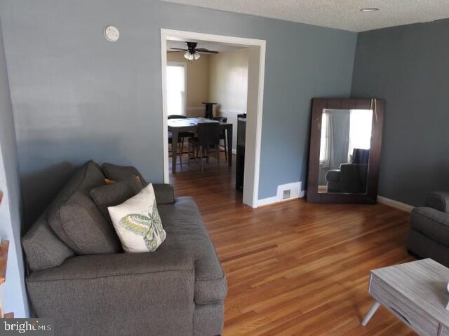 living room with ceiling fan, wood-type flooring, and a textured ceiling