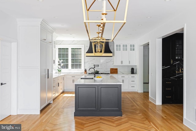 kitchen featuring white cabinetry, tasteful backsplash, a center island with sink, and light parquet floors