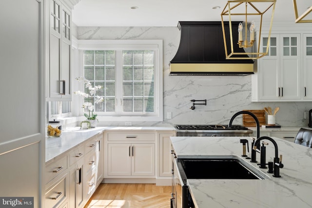 kitchen with pendant lighting, custom range hood, light parquet flooring, white cabinets, and light stone countertops