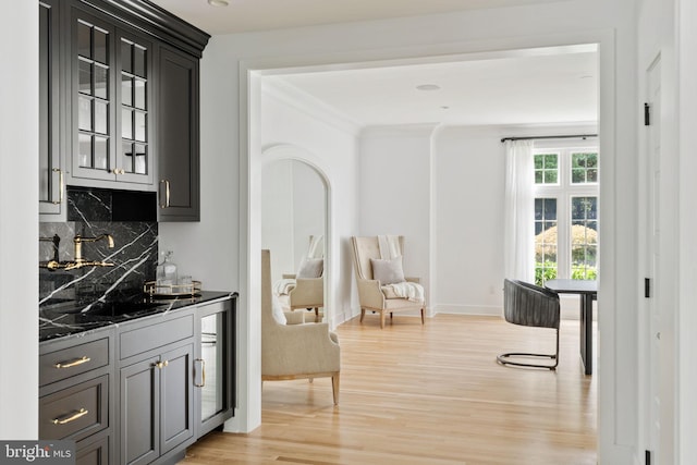 bar featuring light wood-type flooring, crown molding, decorative backsplash, and dark stone counters