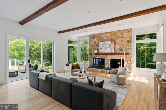 living room with beam ceiling, light hardwood / wood-style floors, and a stone fireplace