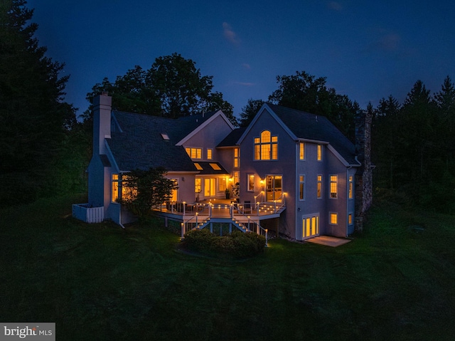 back house at night with a deck and a lawn