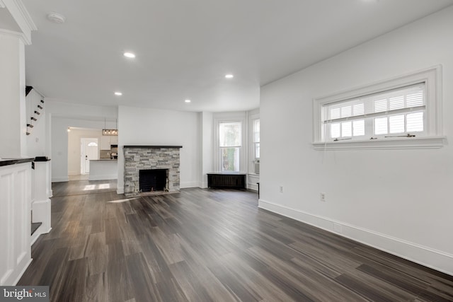 unfurnished living room featuring recessed lighting, baseboards, dark wood-style flooring, and a stone fireplace