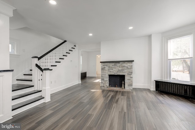 unfurnished living room with radiator, stairs, dark wood-type flooring, and a wealth of natural light