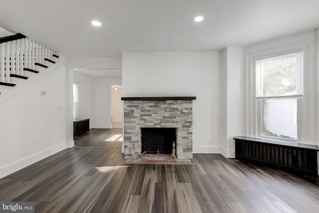 unfurnished living room featuring radiator, a fireplace, baseboards, and dark wood finished floors