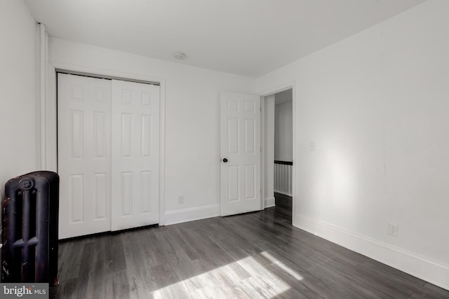 unfurnished bedroom featuring dark wood-type flooring, radiator, and a closet