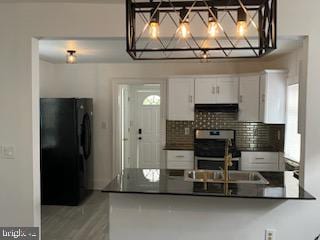 kitchen featuring white cabinetry, tasteful backsplash, black fridge, stainless steel range oven, and kitchen peninsula