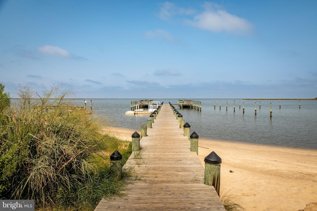 view of dock with a water view and a beach view