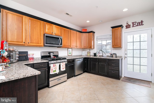 kitchen with light tile patterned flooring, stainless steel appliances, light stone countertops, and sink