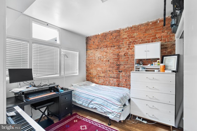 bedroom with brick wall and dark wood-type flooring