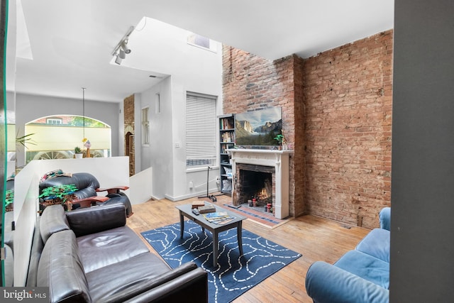 living room with rail lighting, light hardwood / wood-style flooring, a brick fireplace, and brick wall