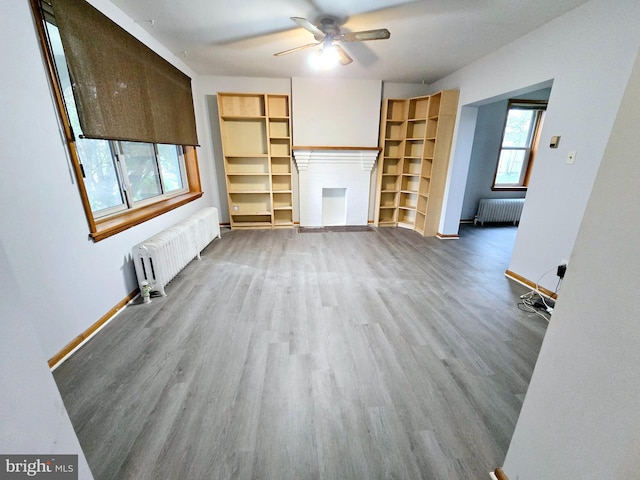 unfurnished living room featuring radiator, wood-type flooring, and plenty of natural light