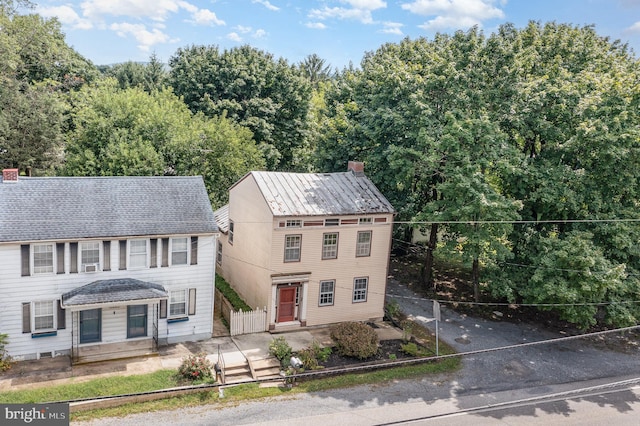 colonial home with a chimney, entry steps, a standing seam roof, fence, and metal roof