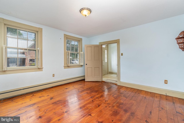 unfurnished room with baseboard heating, wood finished floors, and baseboards