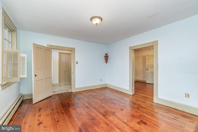 spare room with a baseboard heating unit, baseboards, and wood finished floors