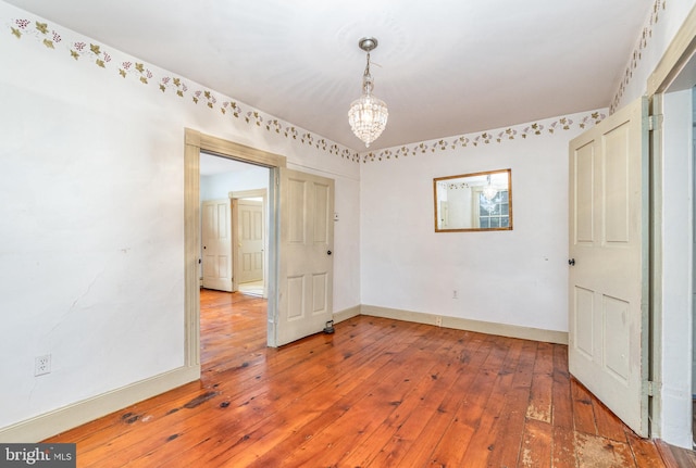 empty room with baseboards, wood finished floors, and an inviting chandelier