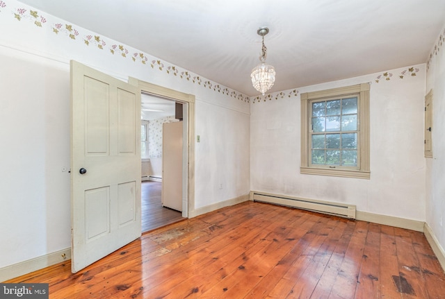 empty room with a baseboard heating unit, an inviting chandelier, baseboards, and wood finished floors