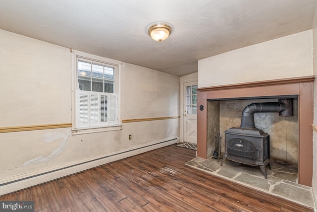 unfurnished living room featuring dark hardwood / wood-style flooring, a baseboard heating unit, and a wood stove