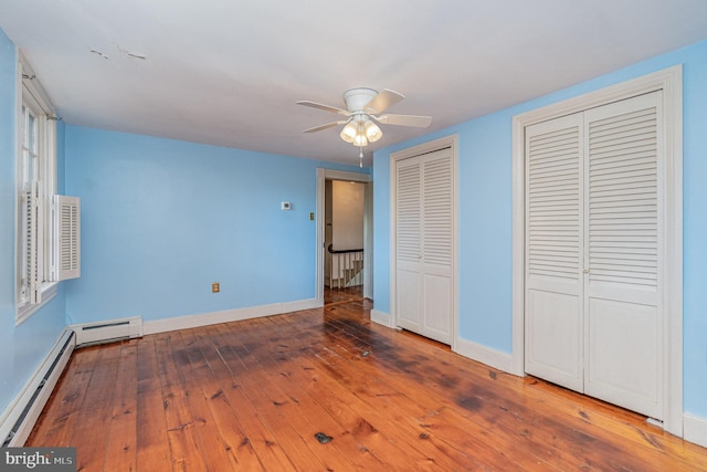 unfurnished bedroom with two closets, wood-type flooring, ceiling fan, and baseboard heating