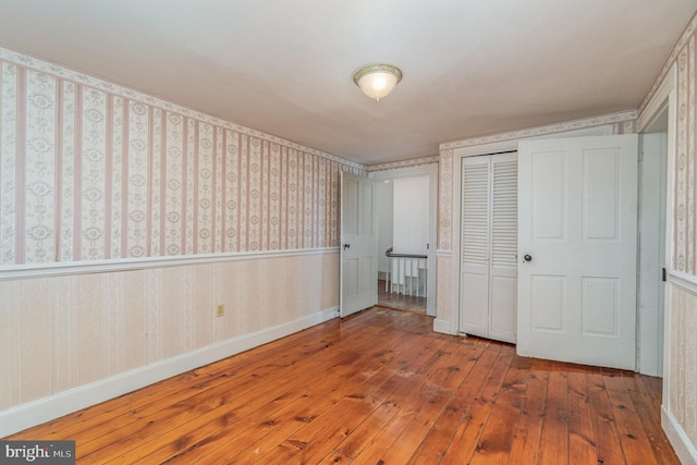 unfurnished bedroom with a wainscoted wall, a closet, wood finished floors, baseboards, and wallpapered walls