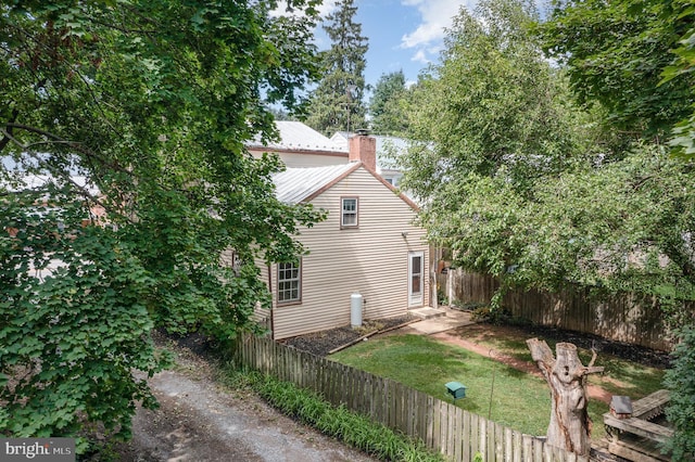 view of property exterior featuring metal roof, a chimney, and fence private yard