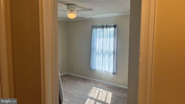 carpeted spare room with a textured ceiling, ceiling fan, crown molding, and plenty of natural light