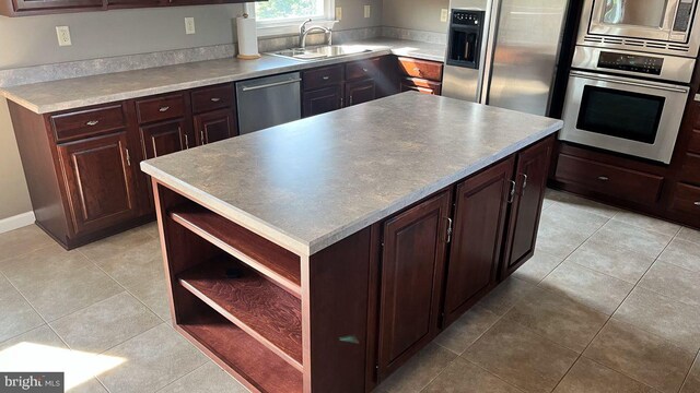 kitchen with sink, light tile patterned floors, a kitchen island, and appliances with stainless steel finishes