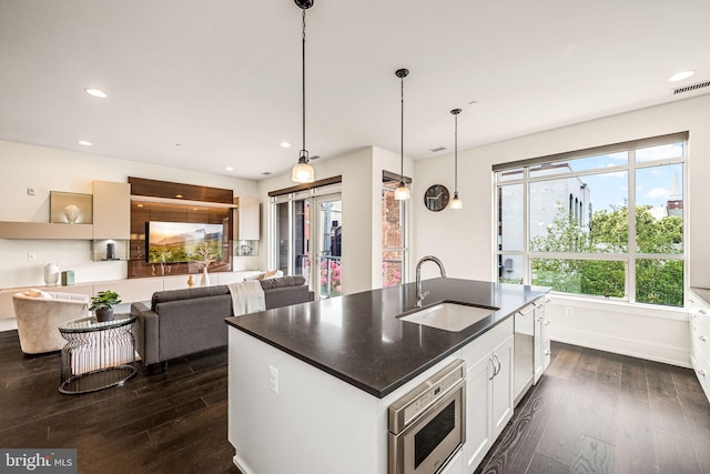 kitchen featuring hanging light fixtures, an island with sink, sink, and white cabinets