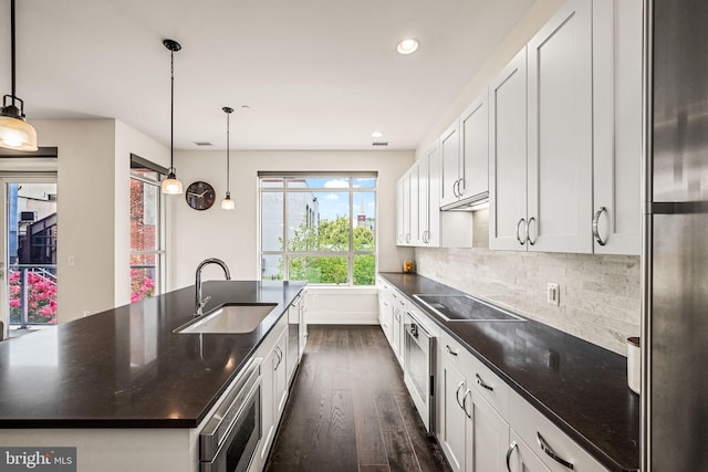 kitchen featuring appliances with stainless steel finishes, pendant lighting, white cabinetry, sink, and a kitchen island with sink