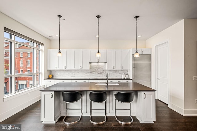 kitchen with sink, decorative light fixtures, an island with sink, white cabinets, and backsplash