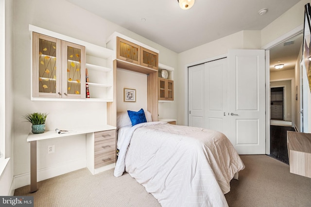 bedroom with light colored carpet, built in desk, and a closet