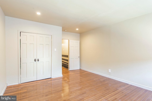 unfurnished bedroom with recessed lighting, a closet, baseboards, and wood finished floors