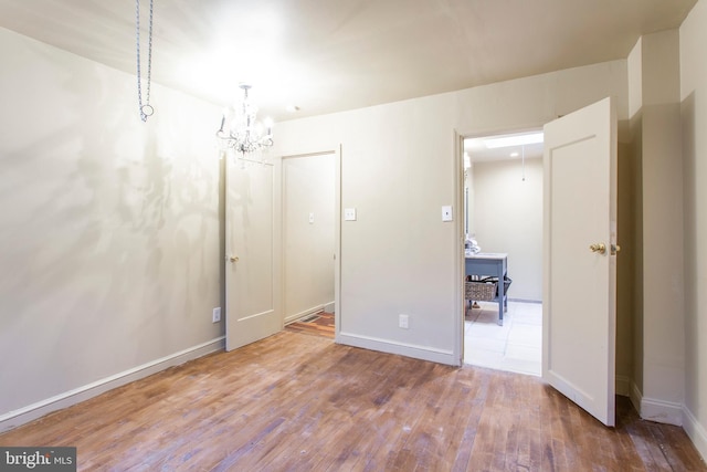 empty room featuring baseboards, a chandelier, and wood finished floors