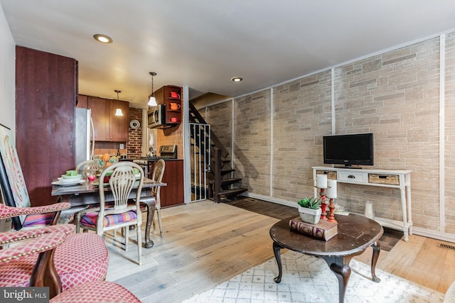 living room with light wood finished floors, brick wall, stairway, and recessed lighting