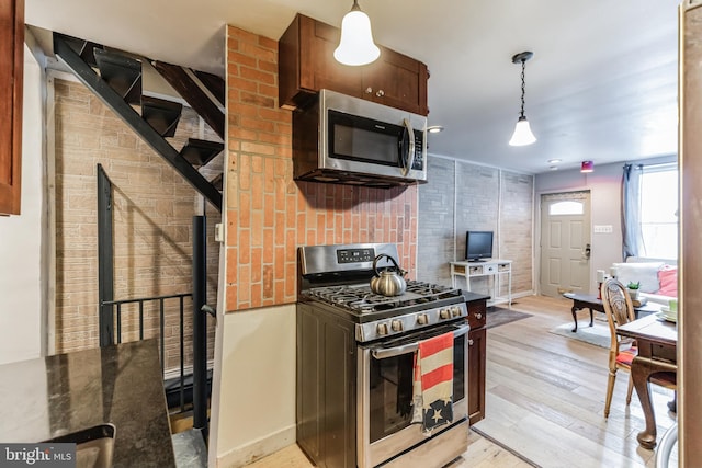 kitchen featuring dark countertops, light wood finished floors, stainless steel appliances, and hanging light fixtures