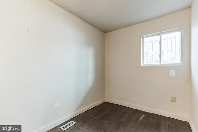 empty room with dark wood-type flooring, visible vents, and baseboards