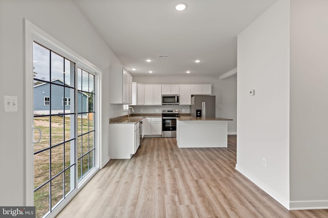 kitchen with sink, white cabinetry, dark stone countertops, stainless steel appliances, and light wood-type flooring