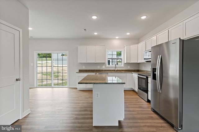 kitchen with sink, stainless steel appliances, white cabinets, a kitchen island, and dark stone counters