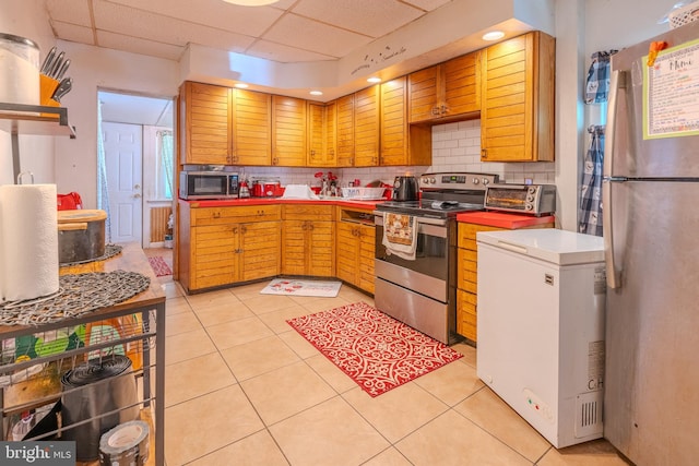 kitchen featuring appliances with stainless steel finishes, a drop ceiling, light tile patterned floors, and decorative backsplash