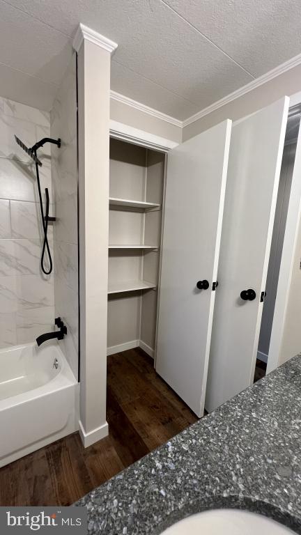 bathroom with hardwood / wood-style floors, crown molding, a textured ceiling, and tiled shower / bath