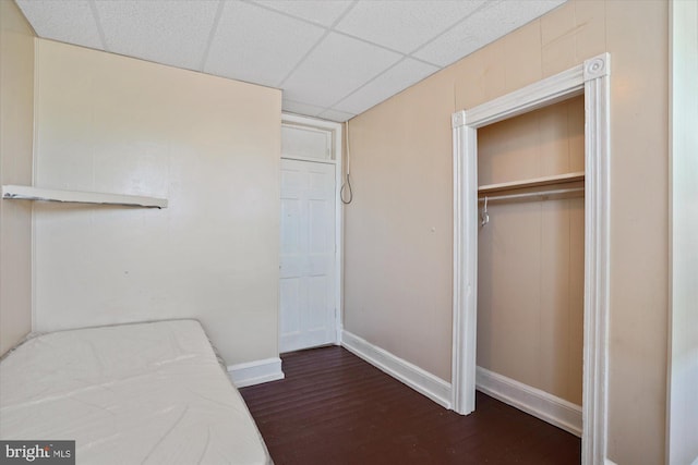 unfurnished bedroom featuring a paneled ceiling, dark wood-type flooring, and a closet