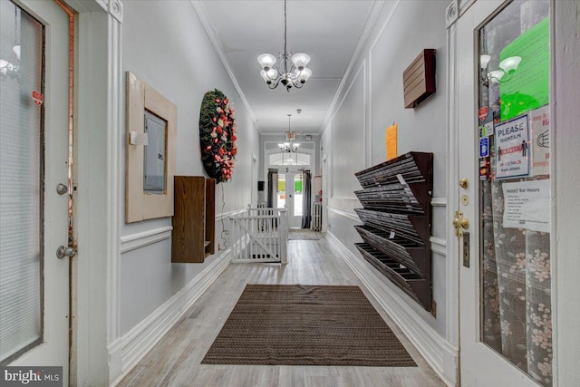 corridor with light hardwood / wood-style flooring, crown molding, and a chandelier